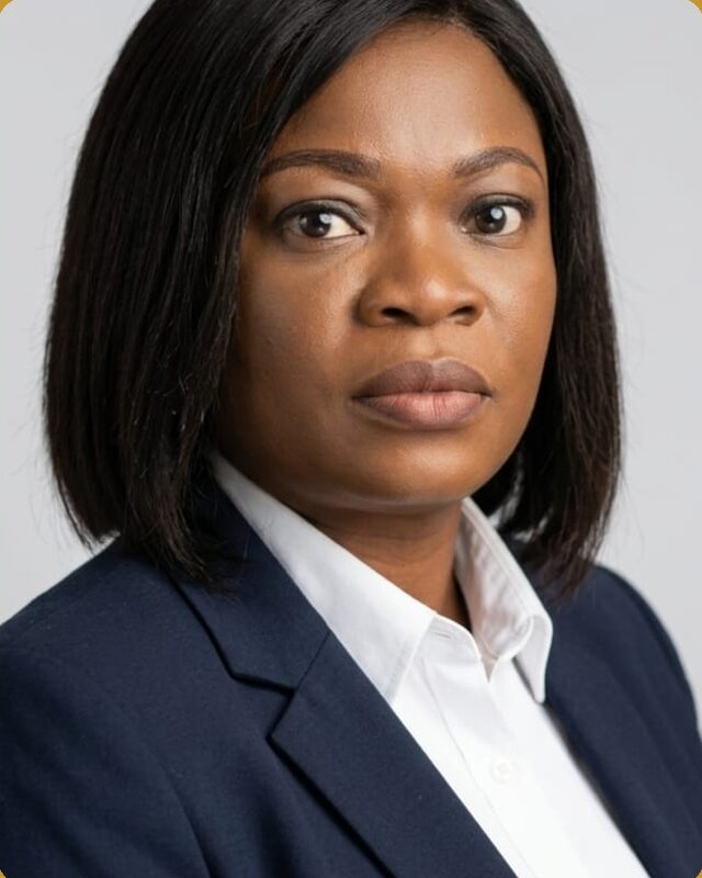 A studio portrait of a woman in a navy blazer and white shirt, against a light grey background.